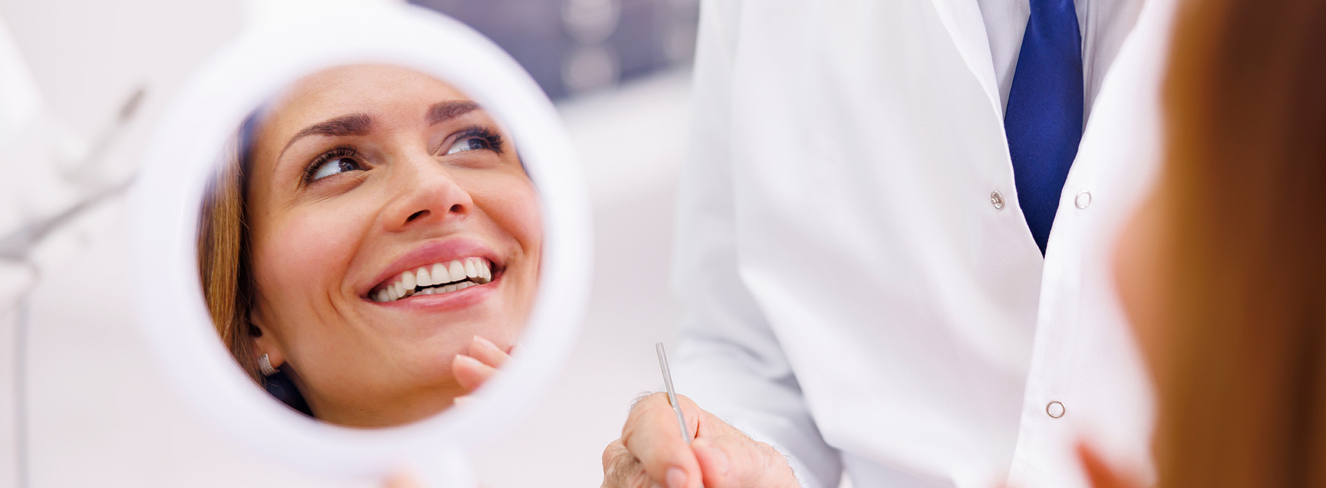A person is seated in a dental chair, receiving care from a dental professional who stands behind them.