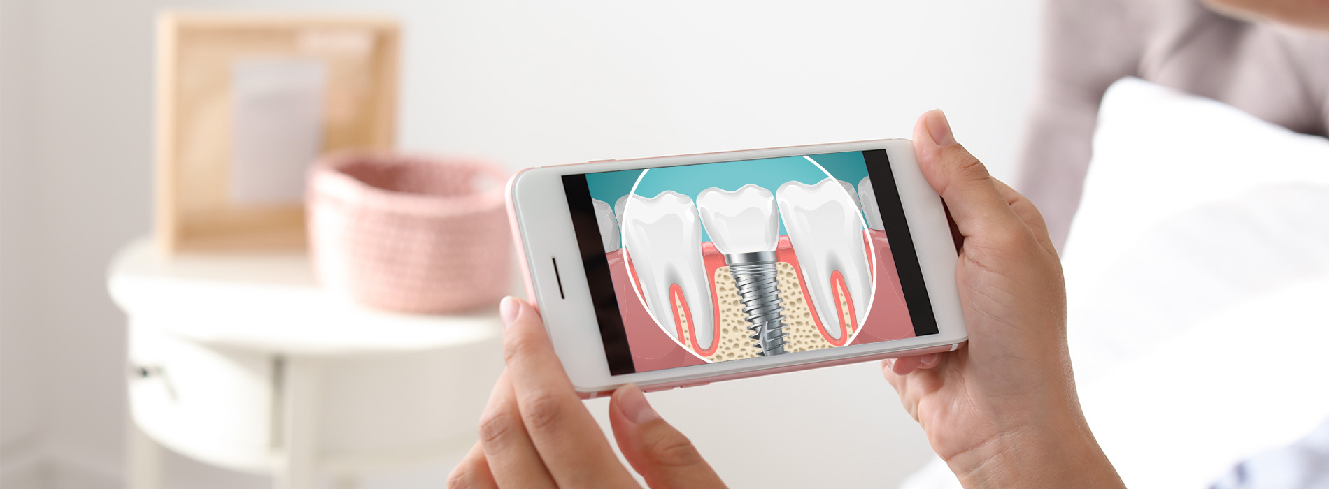 A person holding a smartphone displaying an animated toothbrush cleaning teeth with two hands visible, set against a blurred background featuring a table with items on it.
