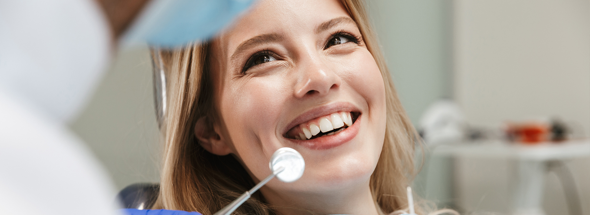 A woman sitting in a dentist s chair with her mouth open, smiling at the camera while looking towards the dental professional who is examining her teeth.