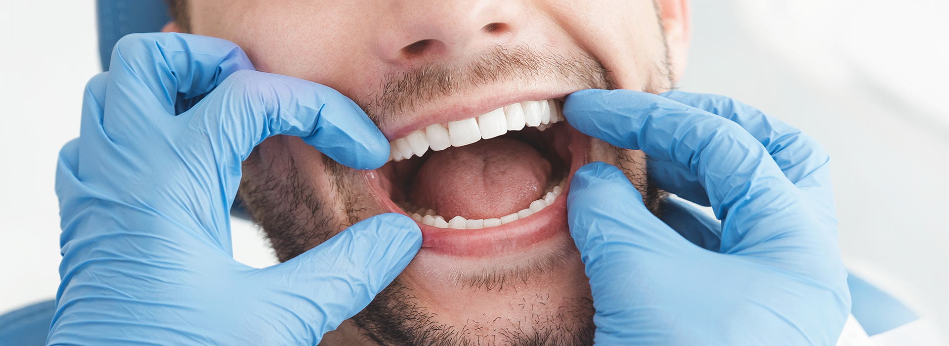 A dental hygienist wearing gloves is performing oral care on a patient s teeth, with the patient s mouth wide open.