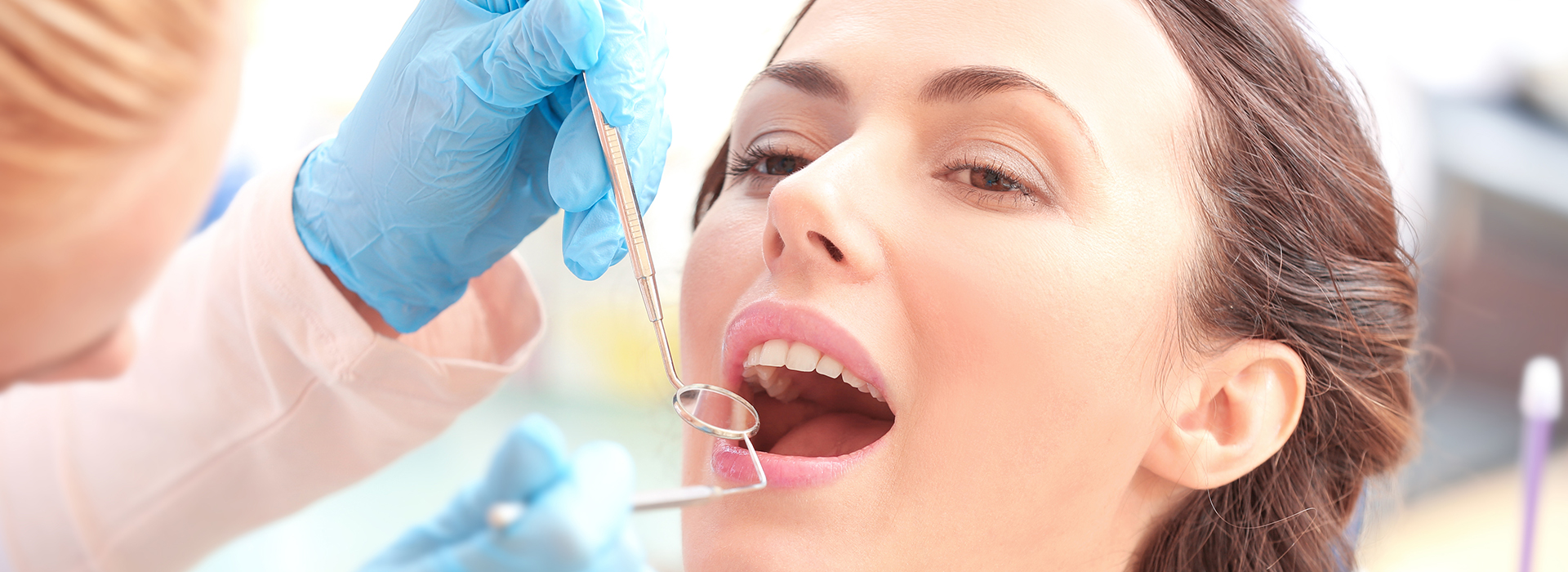 A woman receiving dental treatment with a needle in her mouth, surrounded by medical professionals in a dental office setting.