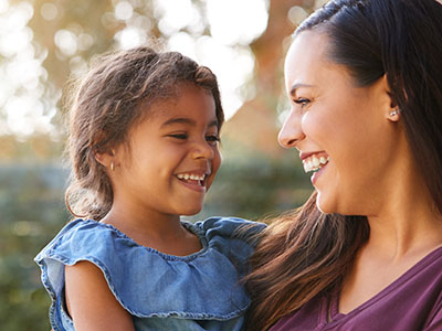 A smiling woman holding a young child with a joyful expression.