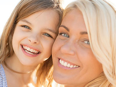 A woman and child are smiling at the camera with a blurred background.