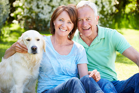 This image features an elderly couple sitting outdoors with their golden retriever dog, posing for a photograph.