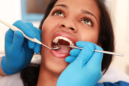 Woman receiving dental treatment with dental instruments visible.
