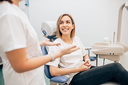 A woman sitting in a dental chair, smiling at the camera, while two dental professionals attend to her.