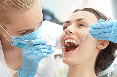 The image shows a dental hygienist performing a procedure on a patient s teeth, with the patient smiling while seated in a dentist s chair.