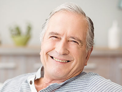 An elderly man with gray hair is smiling and appears relaxed while sitting in an armchair.