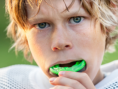 A young boy with blonde hair blowing green bubble gum.